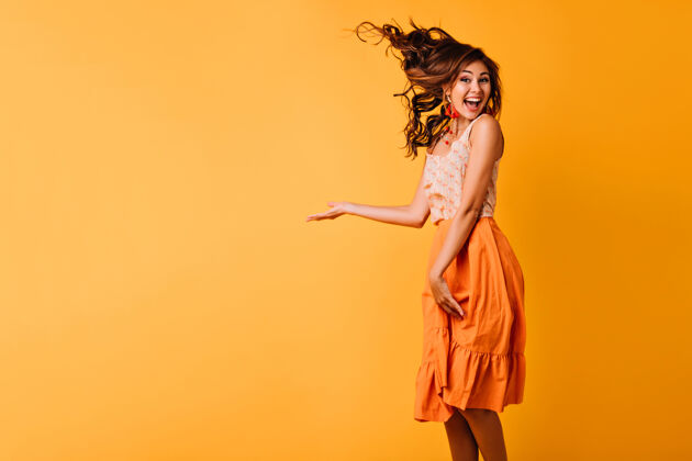 瘦身一头姜黄色卷发的兴奋女孩在黄色的舞台上跳跃身着橙色服装的幸福少女微笑着跳舞的摄影棚写真休闲女性年轻