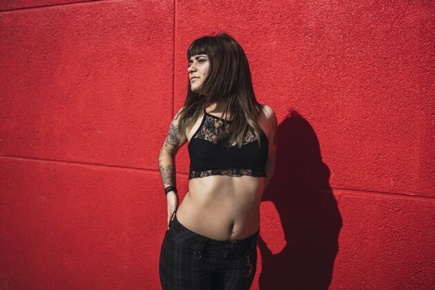 性感年轻漂亮的白种女人站在红墙边纹身黑发吸引力头发