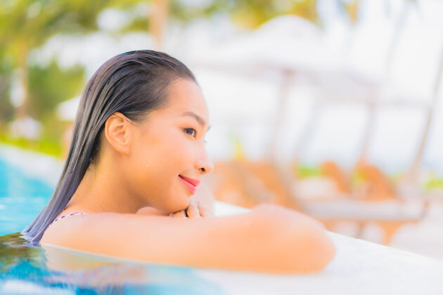 海滩肖像美丽的亚洲年轻女子放松休闲周围的室外游泳池与海洋海滩健康夏威夷度假村
