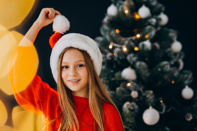 传统可爱的少女戴着圣诞树旁的红色圣诞帽装饰年轻圣诞