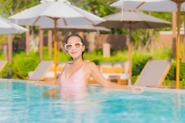 棕褐色肖像美丽的亚洲年轻女子放松休闲围绕室外游泳池与海健康酒店日光浴