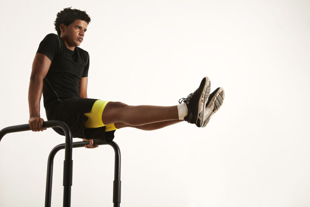 健身房一个穿着黑色运动服的严肃的年轻美籍非洲裔男子在家里靠着白墙坐在短杠上做l型座椅男子健身实践