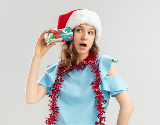 新年一位身穿蓝色上衣 头戴圣诞老人帽 脖子上戴着金属箔的年轻女子 耳边戴着五颜六色的纸杯五颜六色年圣诞