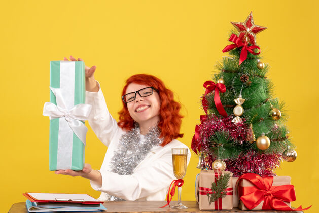 情感前视图：女医生拿着圣诞礼物和黄色背景上的圣诞树坐着人树插花