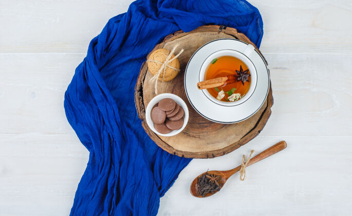 平板一杯茶 棕色和白色的饼干放在木板上 蓝色的围巾和一勺丁香围巾木头丁香