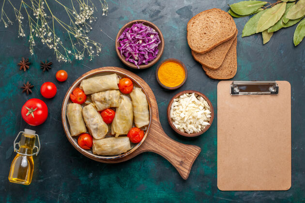 食物俯瞰图美味的肉食卷卷心菜和西红柿称为dolma面包和橄榄油在深蓝色的桌子上西红柿肉橄榄