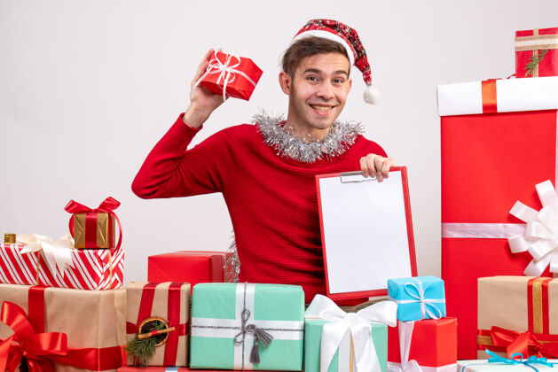 礼物正面图快乐的年轻人拿着剪贴板围坐在圣诞礼物旁边拿着庆祝人