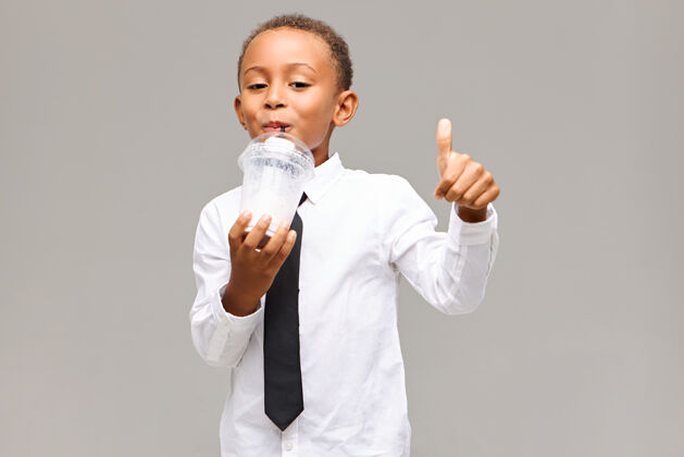 幸福帅气可爱的黑皮肤男学生 穿着白衬衫 打着黑领带 在学校午休时 一边喝着健康的奶昔 一边竖起大拇指 神情愉悦小玻璃能源