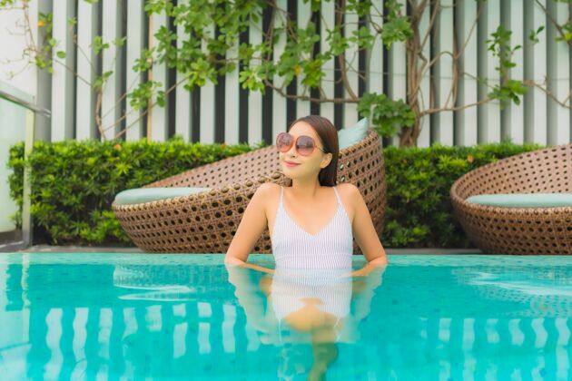 享受肖像美丽的亚洲年轻女子在酒店度假区的室外游泳池周围放松休闲旅游度假太阳镜微笑夏天