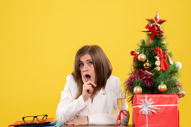 情绪正面图：女医生坐在黄色背景的桌子前 放着圣诞树和礼品盒医院坐着医生