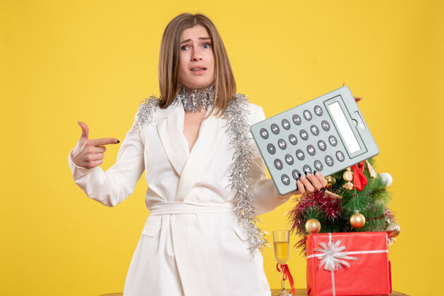 人正面图女医生站着拿着计算器 背景是黄色的圣诞树和礼品盒漂亮快乐圣诞节
