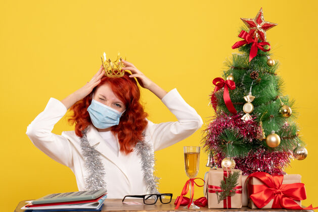 坐前视图女医生戴着面具坐着 圣诞礼物戴着黄色背景的皇冠前面年圣诞节