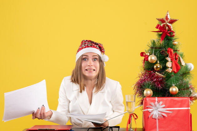圣诞节前视图女医生坐在圣诞礼物持有黄色背景文件医生前面坐着