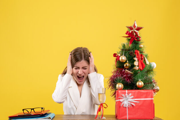 前面正面图：女医生坐在黄色背景的桌子前 放着圣诞树和礼品盒成人男人微笑