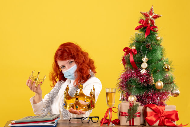 抱着前视图女医生坐在圣诞礼物和举行的黄色背景上的皇冠圣诞节鲜花漂亮