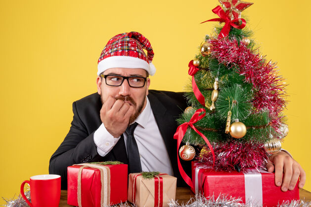 礼物正面图：男性工人坐在他工作的地方后面 黄色办公桌上摆着礼物办公室彩色工作圣诞礼物地点圣诞节工作