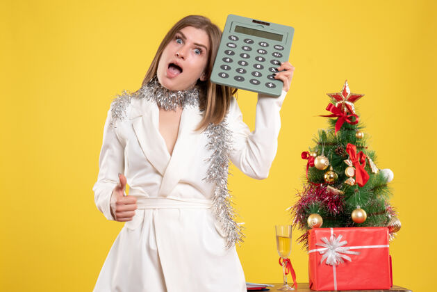 女正面图女医生站着拿着黄色的计算器 还有圣诞树和礼品盒女医生年人