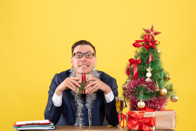 女士微笑的男人坐在圣诞树旁的桌子前 黄色的礼物微笑地方黄色