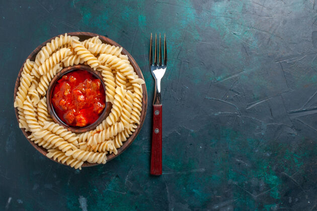 西红柿在深蓝色的桌子上俯瞰着意大利面食和番茄酱甜食美味小吃