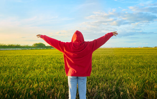 女人特写镜头一个年轻的红衣女子兴高采烈地站在一个阳光明媚的日子在绿地上田地优雅五颜六色