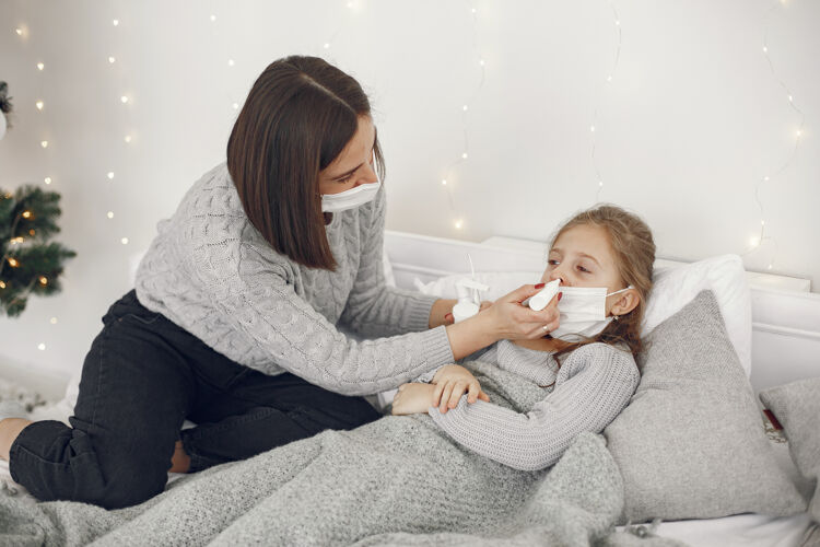 温度儿童中有冠状病毒母亲带着女儿孩子躺在床上戴着医用口罩的妇女年轻妈妈医疗