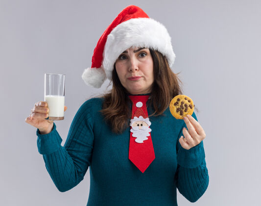 帽子失望的成年白人妇女戴着圣诞帽 打着圣诞领带 手里拿着一杯牛奶和饼干 背景是白色的 还有复印空间快乐杯子领带