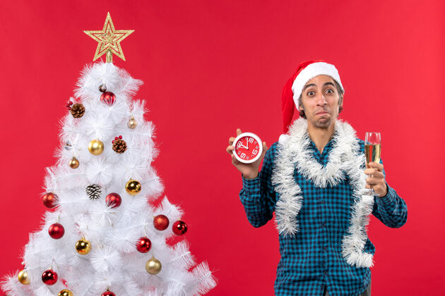 时钟一个戴着圣诞老人帽子 端着一杯酒 拿着钟 充满好奇心的年轻人圣诞小伙子小伙子