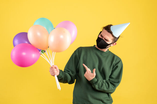 欢乐正面图：戴着派对帽和黑色面具的年轻人指着黄色的气球年轻聚会黑色