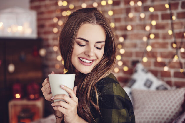 圣诞节时间微笑的女人在家喝咖啡休息一下喝酒休息