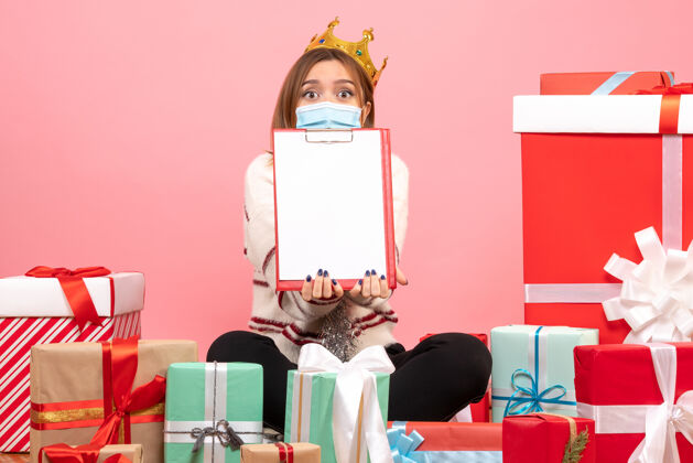 Covid正面图年轻女性围坐在圣诞礼物旁边 带着文件便条便条粉色圣诞节
