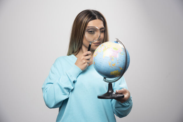 地理穿着蓝色运动衫的金发女孩拿着一个地球仪 用放大镜寻找目的地世界显微镜成人