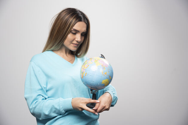 年轻穿着蓝色运动衫的金发女孩手里拿着地球仪 仔细地查看着地球地图目的地休闲学习