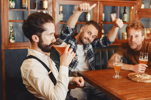 交谈和最好的朋友见面三个穿着休闲服的快乐的年轻人一起坐在酒吧里聊天喝啤酒人类饮酒男性