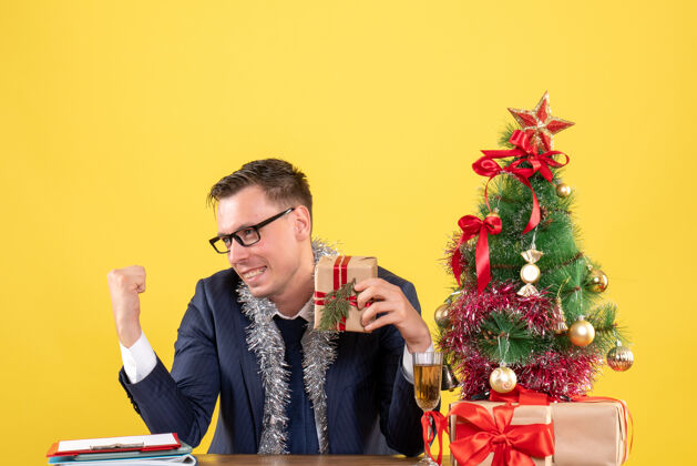 黄色正面图：快乐的年轻人坐在圣诞树旁的桌子旁 黄色的礼物年轻人男性快乐