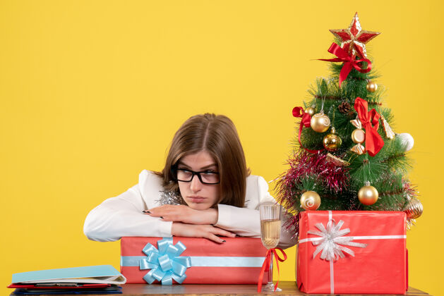 礼物正面图女医生坐在桌子前 拿着礼物 黄色的圣诞树和礼盒女医生家圣诞节