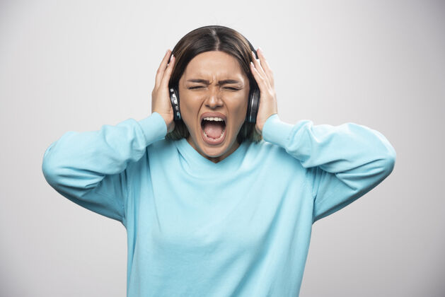 年轻穿着蓝色运动衫的金发女孩听着耳机 不喜欢音乐人类消极人