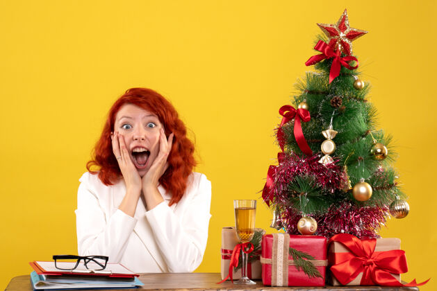 人前视图：女医生坐在桌子后面 拿着圣诞礼物 黄色背景上的圣诞树健康礼物医院