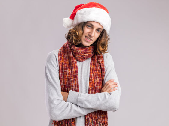 脸快乐而积极的年轻人戴着圣诞老人帽 脖子上围着温暖的围巾 双臂交叉 面带微笑快乐快乐年轻
