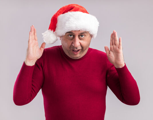 测量中年男子戴着圣诞老人的帽子看着相机惊讶地用手做着大小的手势象征测量站在白色背景上圣诞老人手势大小