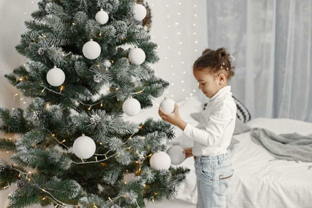 房间穿白色毛衣的孩子站在圣诞树旁的女儿室内肖像圣诞节
