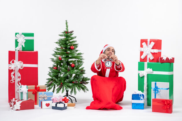 庆祝年轻人坐在地上 在礼物和圣诞树旁展示圣诞钟 庆祝圣诞节装饰礼物年轻人
