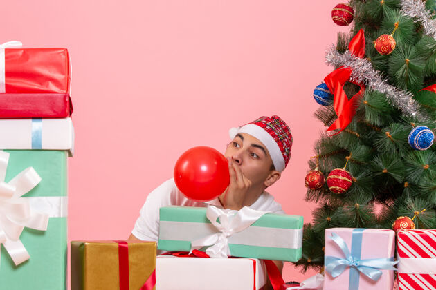 盒子一个年轻人庆祝圣诞礼物周围的粉红色墙上的前视图快乐圣诞节庆祝