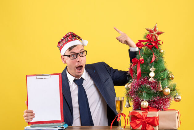 桌子前视图奇怪的商人坐在圣诞树附近的桌子上 黄色的礼物行政人员男性树