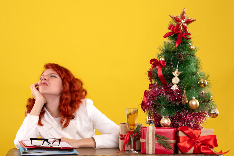 办公室女工人坐在桌子后面 拿着圣诞树和黄色的礼物桌子女手镯