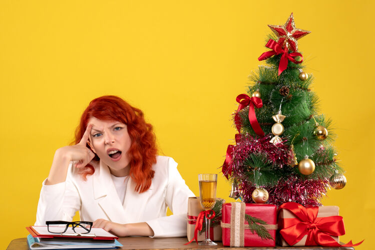 圣诞节女工人坐在桌子后面 手里拿着圣诞礼物和黄色的圣诞树女人桌子