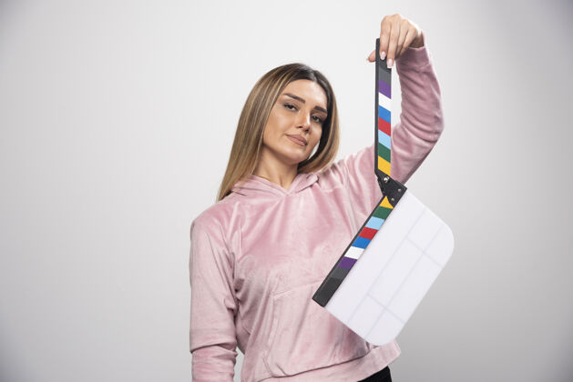 女性穿着粉色运动衫的金发女士拿着一块空白的隔板 摆出积极有趣的姿势电影制作电影电影