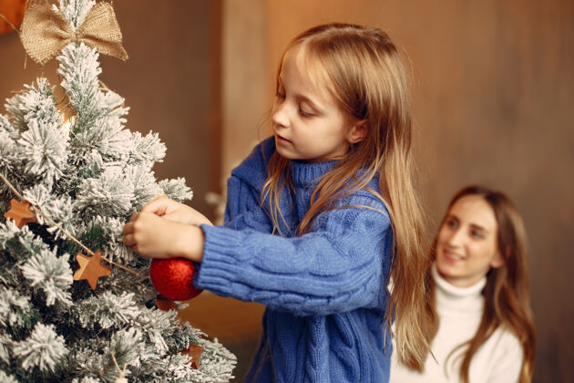 树人们在为圣诞节做准备母亲在和女儿玩耍一家人在节日的房间里休息孩子穿着蓝色毛衣玩具给女人