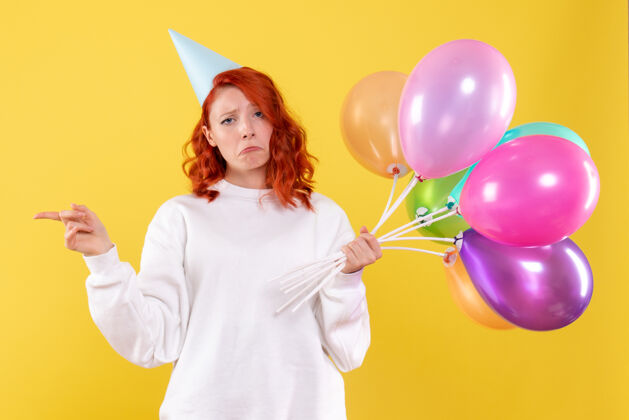 聚会黄色墙壁上手持彩色气球的年轻女子的正视图庆祝气球生日