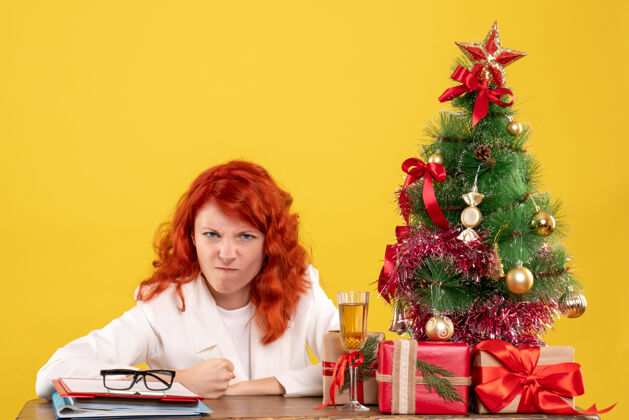 插花前视图：女医生坐在桌子后面 黄色背景上有圣诞礼物女医生人花