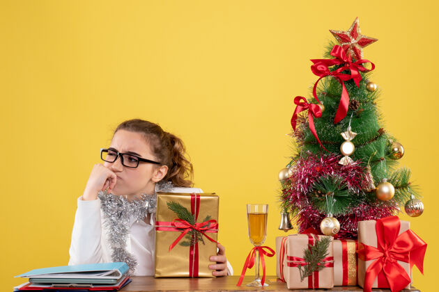 女医生前视图女医生围坐在圣诞礼物和浅黄色背景上的树思考情感女性新郎